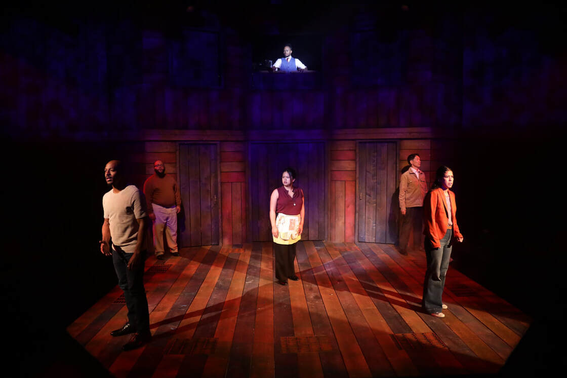 5 people stand on wooden stage, while a 6th person views them from above
